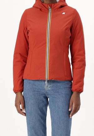 Red hooded jacket with front zipper, elastic cuffs, and side pockets, worn with blue denim jeans on a standing person.