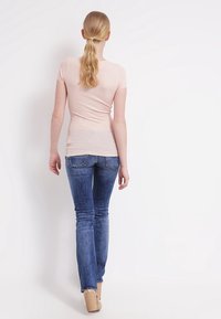 Ljusrosa tajt t-shirt med korta ärmar, i kombination med blå utsvängda jeans. Håret är uppsatt i en hästsvans, sedd bakifrån.