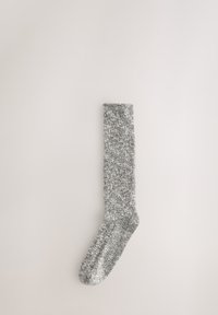 Chaussette montante en tissu tricoté avec un motif gris et blanc chiné. Elle présente un bord-côte côtelé et une zone d'orteils lisse.