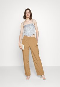 Světlomodrý cropped top s paisley vzorem a tenkými ramínky, zkombinovaný s béžovými kalhotami s vysokým pasem a širokými nohavicemi. Model drží krémovou kabelku.