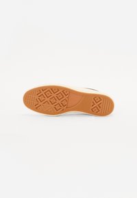 Semelle en caoutchouc marron avec un motif texturé comprenant des diamants et des lignes. Bord clair avec des accents beige, conçu pour une meilleure adhérence.