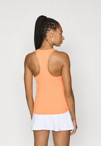 Orange racerback tank top made from a stretchy fabric, paired with a white skirt. The back features a smooth, streamlined design.