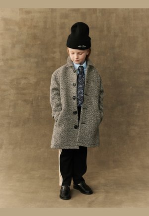 Grijs houndstooth jas met knopen, zwarte beanie, blauwe shirt, gestreepte stropdas, zwarte broek met witte strepen en zwarte schoenen.