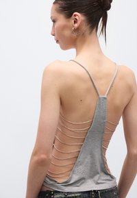 Halli top, millel on õhukesed spagetirihmad ja sügav seljaosa lõige, horisontaalse hõbedase kettakujundusega ja pehme tekstuuriga.