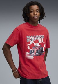 Rød bomulds T-shirt med teksten "Scuderia Ferrari" og et grafisk motiv af en Ferrari racerbils. Korte ærmer og afslappet pasform.