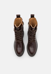 Brown leather ankle boots with a smooth finish, featuring lace-up front, contrasting tan interior, and a pull tab on the back.