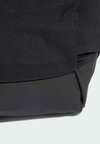 Zaino in tessuto nero con una texture liscia, forma strutturata e parte superiore ripiegata. La sezione inferiore ha una finitura opaca.