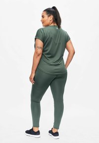 Olive green athletic top with short sleeves and matching leggings. Smooth texture, fitted design, and paired with black sneakers.