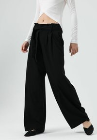 Zwarte wijde broek met hoge taille, voorzien van plooien en een bijpassende stoffen riem. Gladde textuur, op maat gemaakte uitstraling en minimale accenten.