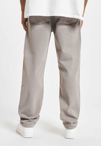 Pantalones de mezclilla gris claro con un ajuste relajado, que cuentan con bolsillos traseros y dobladillos acampanados. Combinados con zapatos blancos, mostrando una textura suave.