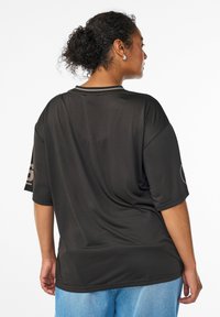 Schwarzes, oversized T-Shirt mit kurzen Ärmeln, aus einem atmungsaktiven Mesh-Material gefertigt. Es hat einen runden Halsausschnitt und Logo-Akzente an den Ärmeln.