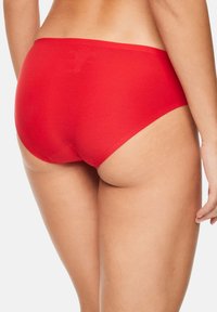 Rode bikini slip van soepel stof, met een lage taillehoogte en minimale bedekking. Naadloze randen en een eenvoudig ontwerp zonder zichtbare hardware of patronen.