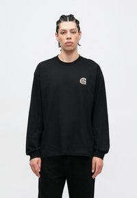 Schwarzes langärmeliges T-Shirt aus Baumwolle mit einem kleinen gestickten Logo auf der linken Brustseite. Einfaches Design, rundhalsausschnitt.