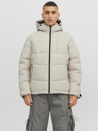 Hellbeige Puffer-Jacke mit Kapuze, ausgestattet mit einem Frontreißverschluss, schwarzen Akzenten und einem gesteppten Muster. Kombiniert mit grauen Cargo-Hosen.