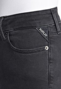 Mustat farkut, joissa on kapea malli, näkyvät saumat ja pieni logo-ämpäri etutaskussa. Hopeiset yksityiskohdat.