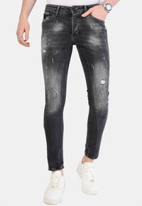 Zwarte skinny jeans met versleten details, verfvlekken en een strakke pasvorm. Gecombineerd met witte sneakers.