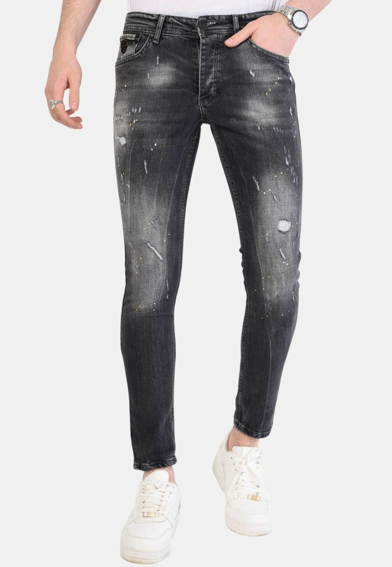 Zwarte skinny jeans met versleten details, verfvlekken en een strakke pasvorm. Gecombineerd met witte sneakers.