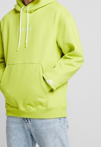 Limonková mikina s kapucí a přední kapsou, bílé šňůrky a vyšívané logo "Just do it."; má malé bílé logo Nike na manžetě.