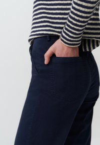 Marineblauwe broek met een slim fit, voorzien van een achterzak en een gladde textuur. Een gestreepte gebreide trui in marineblauw en crème bedekt de bovenkant.