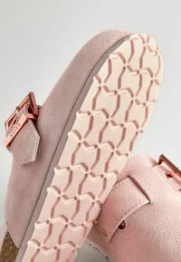 Ljust rosa mockaskor med slip-on-design, featuring en texturerad gummi-sula med ett geometriskt mönster och en detalj i metallspänne.