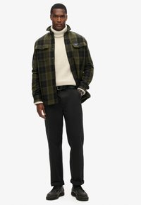 Camisa de franela a cuadros en verde y negro, cuello alto crema, pantalones negros, zapatos de cuero texturizados, reloj de plata, ajuste relajado.