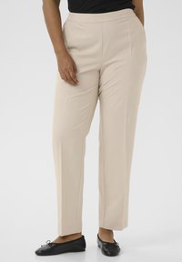 Beige tailored pants with a smooth texture, straight legs, and a mid-rise waistband. Paired with black flats featuring bow accents.