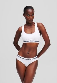 Ensemble en coton blanc composé d'un soutien-gorge et d'un bikini avec une ceinture noire « Karl Lagerfeld », présentant un décolleté carré et un design minimaliste. Texture lisse.