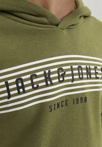 Sudadera verde oliva de algodón, con franjas blancas y marinas que presentan el texto "JACK & JONES" y "SINCE 1990" impreso de manera prominente.