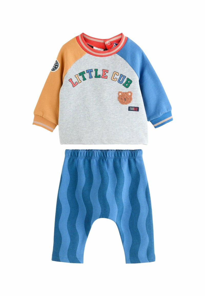 Zweiteiliges Kinderoutfit mit einem grauen Pullover mit mehrfarbigen Ärmeln, dem Text 'LITTLE CUB' und blauen Hosen mit wellenförmigem Muster.