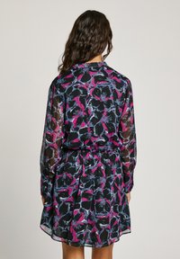 Robe florale avec de longues manches transparentes, base noire, motifs rose et bleu audacieux, taille élastique et coupe décontractée avec un ourlet arrondi.