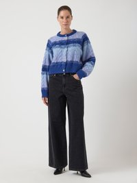 Krajkový úpletový cardigan ve světle a tmavě modrých odstínech s kulatým výstřihem a zapínáním na knoflíky, v kombinaci s černými širokými džíny s vysokým pasem.
