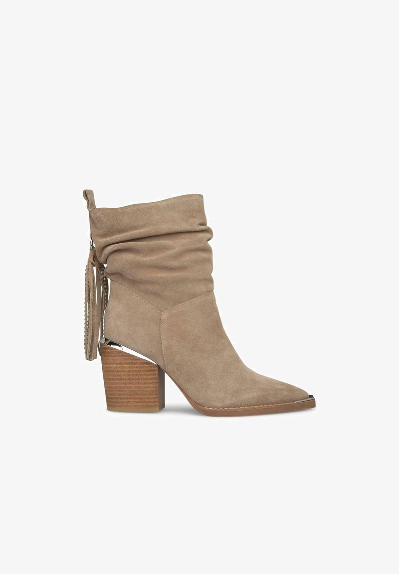 Botín de ante beige con caña caída, punta afilada y tacón de bloque de madera marrón. Presenta un detalle de borlas en el lateral.