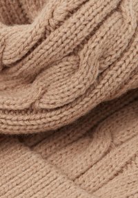 Close-up van beige gebreide stof met dikke kabel- en ribbelsteekpatronen die een zachte textuur en gedetailleerde garenstrengen tonen.