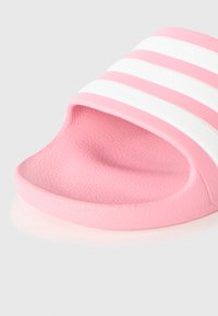 Ružová šľapka so štruktúrovanou gumou, s tromi bielymi horizontálnymi pruhmi na hornej časti a zaobleným otvorom na prsty.