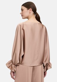 Satinbluse in Hellrosa mit lockerer Passform, weitem Halsausschnitt und gerafften Bündchen. Glatte Textur und lange Ärmel sind vorhanden.