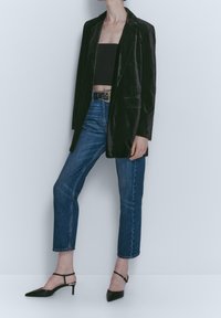 Blazer en velours noir avec revers crantés, porté sur un haut court, associé à un jean taille haute bleu et des escarpins slingback noirs à bout pointu.