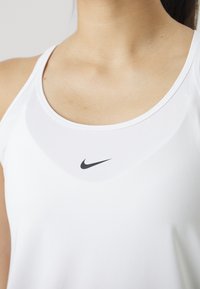 Gros plan d'une personne portant un haut de sport blanc sans manches avec un petit logo Nike noir centré près de l'encolure.