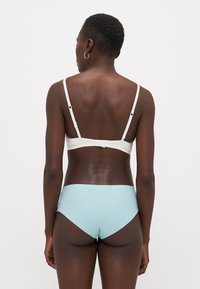 Fehér bikini felső vékony pántokkal, egyszerű, sima dizájnnal. Világoskék, magas derekú bikini alsó, varrás nélküli szélekkel és minimális részletezéssel.