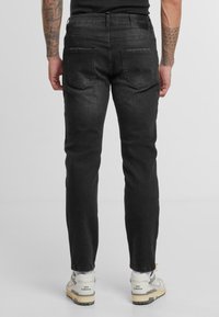 Vaqueros de mezclilla negros de corte ajustado, con dos bolsillos traseros y un ligero desgaste. Combinados con zapatillas grises y blancas.