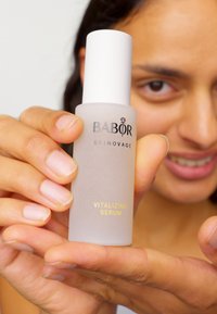 Bottiglia in vetro satinato con un tappo bianco, etichettata "BABOR SKINOVAGE SIERA VITALIZZANTE" in testo nero e oro, tenuta in mano.