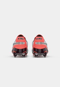 Red and silver soccer cleats featuring a sleek design, textured upper, and black sole with multiple spikes for traction. "KING" branding on heels.