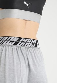 Svart sport-bh med silverfärgad band och logotyp; grå shorts med ett tjockt, svart midjeband som har upprepande vit varumärkesbokstäver.