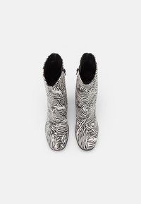 Knee-high buty w wzór zebry w czarno-białym kolorze, o gładkiej fakturze i z bocznymi zamkami ułatwiającymi zakładanie.