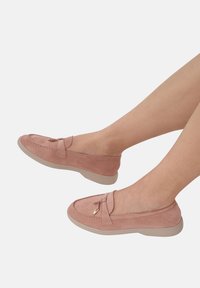 Różowe zamszowe mokasyny z płaską beżową podeszwą, z ozdobnym detalem w postaci zaszewki i subtelnymi stębnowaniami wzdłuż krawędzi.