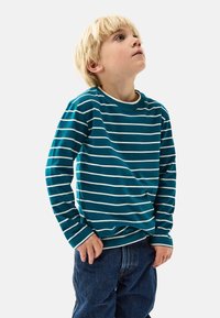 Turkoosi pitkähihoinen paita, jossa on valkoisia vaakasuoria raitoja, pyöreä kaula-aukko ja ribbauskutin. Yhdistetty sinisiin farkkuihin.