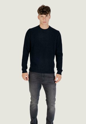 Maglione a coste blu scuro con scollo rotondo, abbinato a jeans grigi. Il tessuto appare morbido, con maniche lunghe e una vestibilità aderente.
