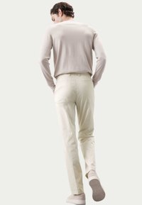 Helles beiges Langarmshirt kombiniert mit hellen Cremefarbenen Hosen. Das Outfit zeichnet sich durch eine lockere Passform, glatte Textur und minimalistisches Design aus.