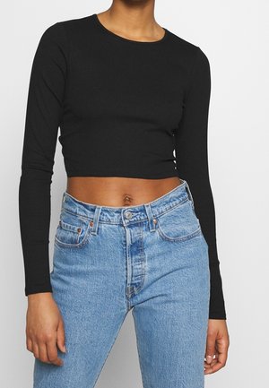 Černý žebrovaný crop top s dlouhým rukávem ve spojení s vysokým pasem světlých modrých džín. Látka vypadá měkce; top má kulatý výstřih.