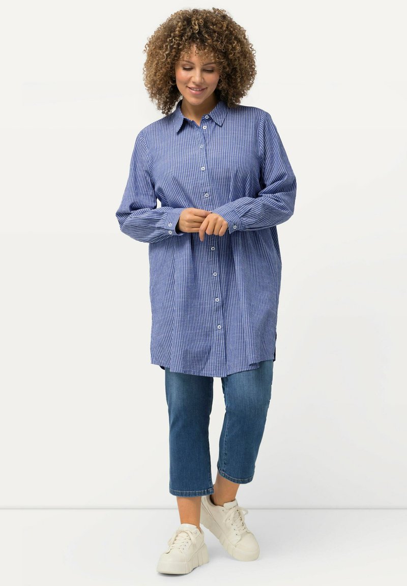 Camicia a maniche lunghe a righe blu e bianche con bottoni, vestibilità rilassata, abbinata a jeans in denim cropped e sneakers bianche.