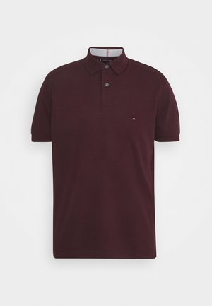 Polo à manches courtes de couleur bordeaux foncé avec patte de boutonnage à deux boutons et petit logo rouge, blanc et bleu sur la poitrine gauche.